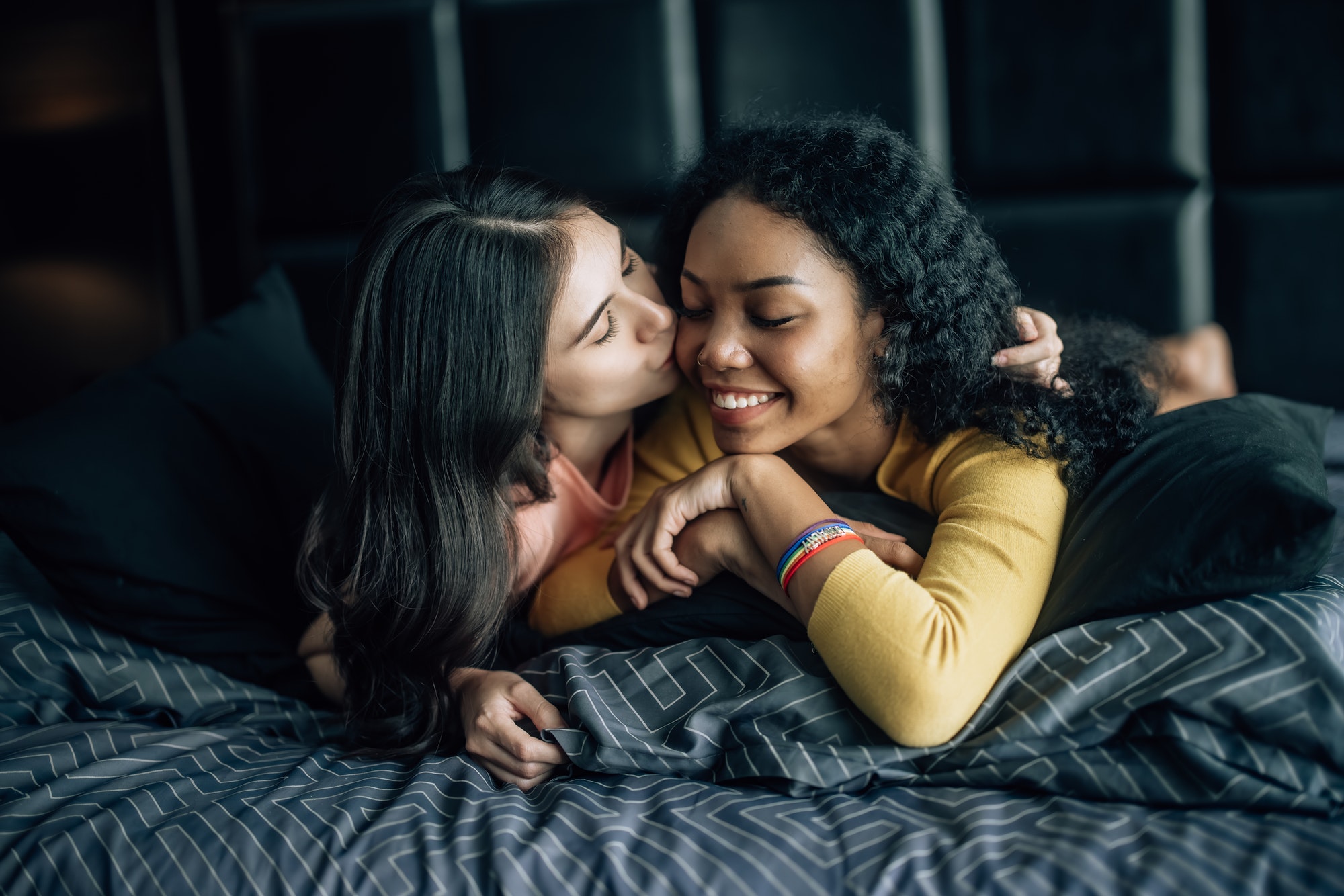 Lesbian partners share joy, play on bed, embrace, exchange tender kiss, radiating genuine happiness