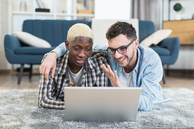 Two multiracial gays using laptop while resting at home