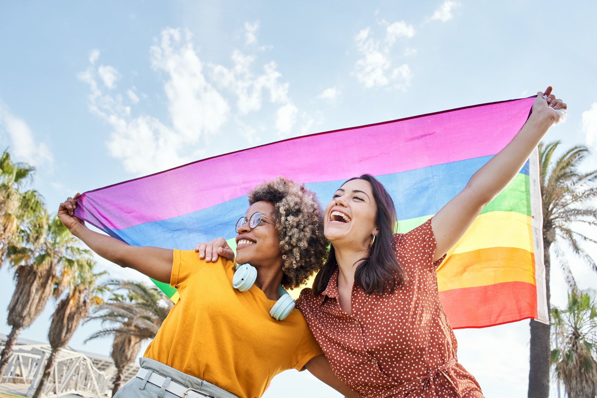 Young lesbian couple celebrates pride day with rainbow flag. Concept of homosexuality, gay.