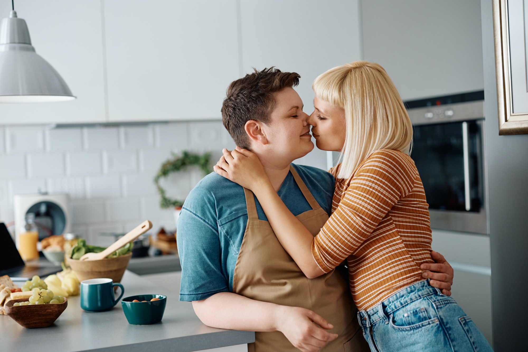 Affectionate lesbian couple kissing in the kitchen.